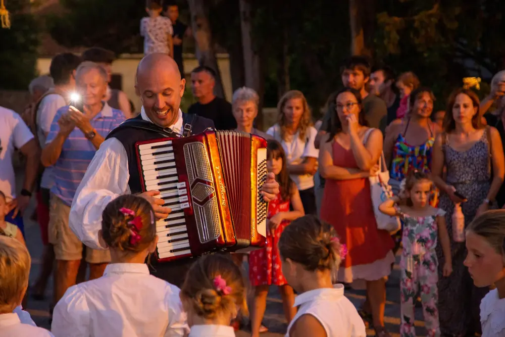 Harmonikaš u nošnji svira okružen djecom i publikom.