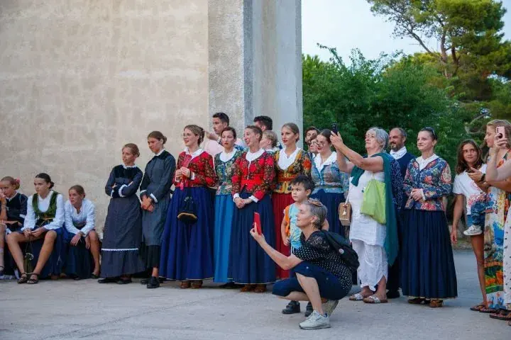 Odrasle plesačice i plesači u nošnjama stoje u redu uz crkvu.