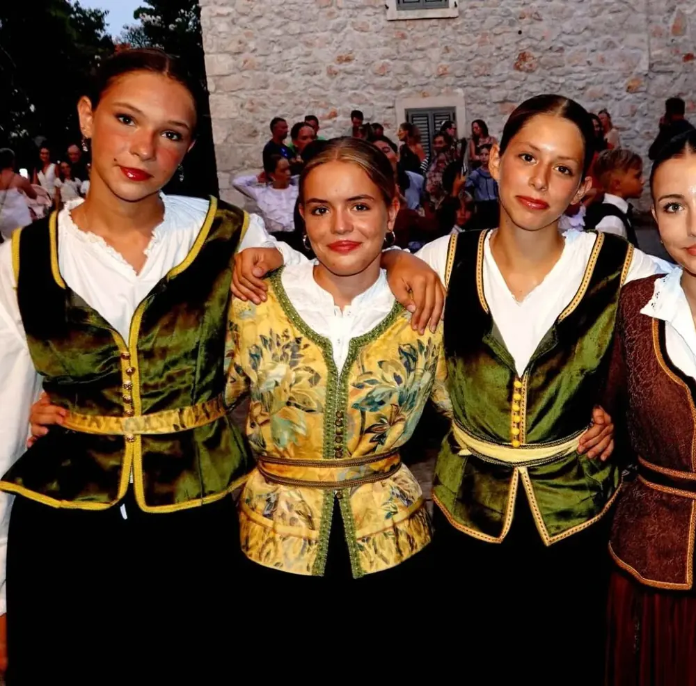 Mlade plesačice u svečanim kaputićima od zelenog, zlatnog i smeđeg brokata s pojasom.