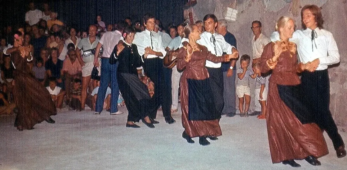 Stara fotografija: plesači u smeđim i tamnim nošnjama plešu u parovima pred mještanima.