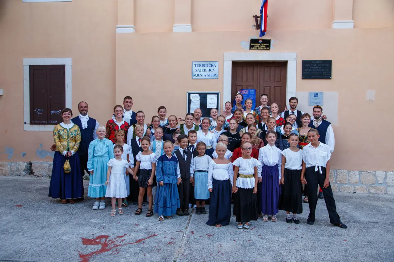 Skupna fotografija djece i odraslih plesača u nošnjama ispred zgrade u Silbi.